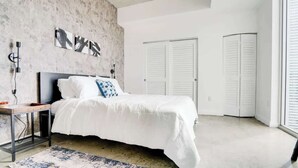 Ein modernes Schlafzimmer mit Bett, Nachttisch, einer Wand aus Beton und einem großen Fenster.