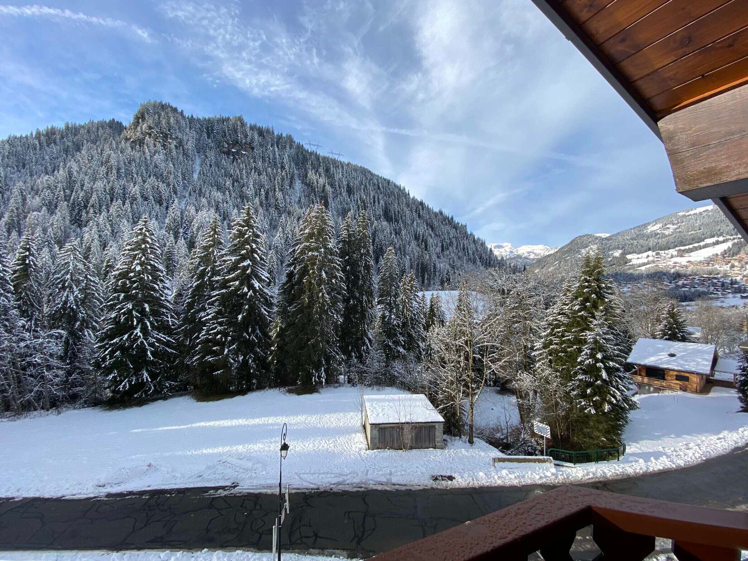 A snowy landscape with a cabin, a clear sky, and a forested mountain in the background.