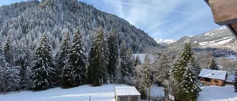 A snowy landscape with a cabin, a clear sky, and a forested mountain in the background.