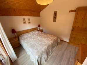 A bedroom with a wooden ceiling, a bed with a patterned bedspread, two bedside tables with lamps, and a wooden wardrobe. - Peaceful apartment in Châtel with WiFi and parking (Châtel)