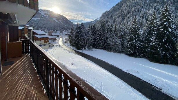 Un paysage montagneux enneigé avec une rivière, des bâtiments et une terrasse en bois.