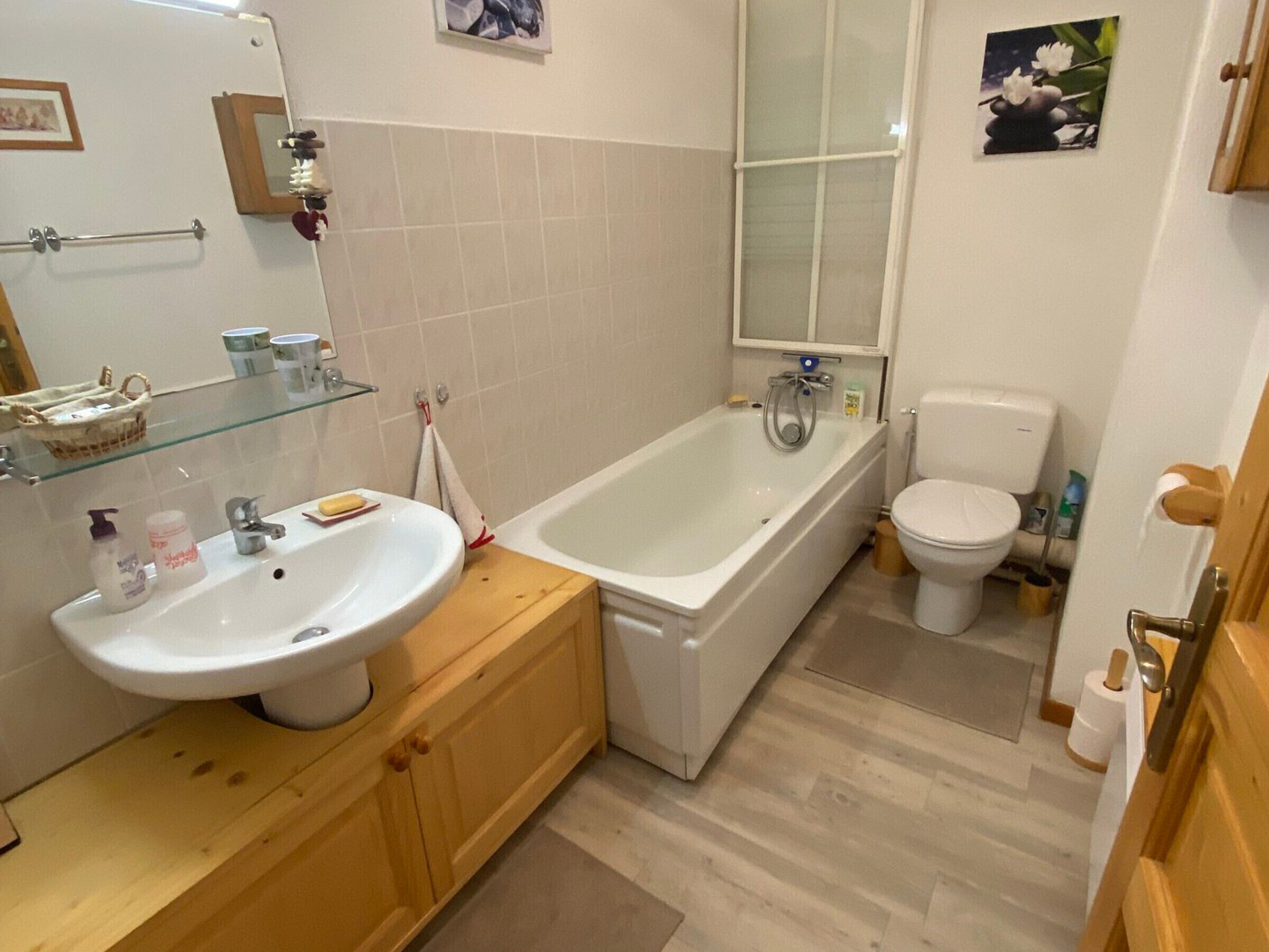 A bathroom with a sink, mirror, bathtub, toilet, and wooden cabinets.