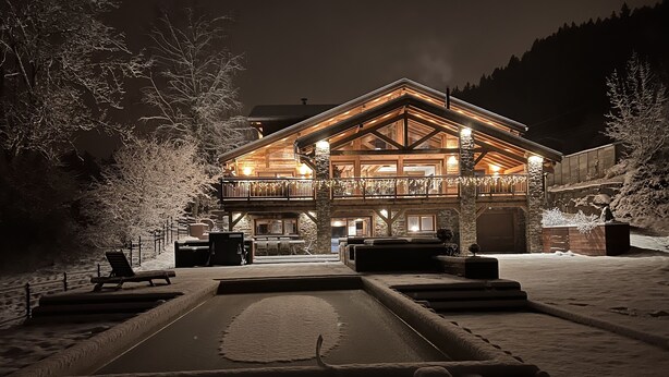 Un espace extérieur enneigé avec un bâtiment en bois doté d’un balcon et d’un mur en pierre.