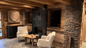 Une pièce chaleureuse avec une cheminée en pierre, des poutres apparentes et deux fauteuils moelleux.