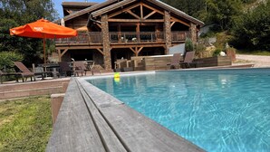 Une terrasse en bois avec une piscine, des chaises longues et un parasol orange.