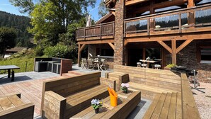 Une terrasse en bois avec coin salon extérieur, un barbecue et une vue panoramique sur les montagnes.
