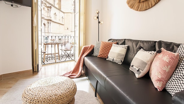 A modern living room with a leather sofa, a woven ottoman, and a large mirror. - Charming Apartment Next to Málaga Cathedral with A/C and Free WiFi (Málaga)