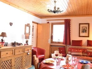 Une pièce chaleureuse avec un plafond en bois, une table à manger dressée avec des assiettes et des verres, un canapé rouge et un buffet en bois doté de tiroirs.