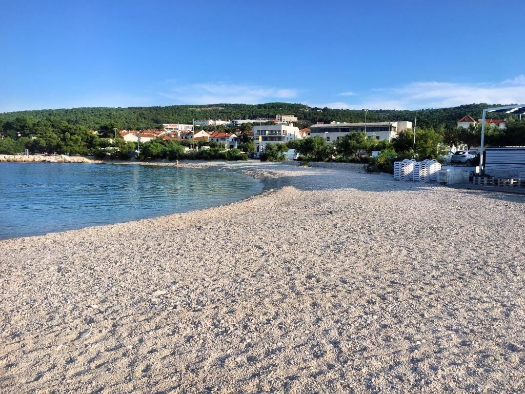 A beach with a clear view of the sea, a sandy shore, and buildings in the background.
