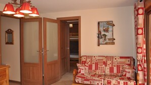 A room with a wooden door, a red and white patterned sofa, a painting on the wall, and a chandelier. - 3-room apartment with large balcony, parking (La Chapelle-d'Abondance)