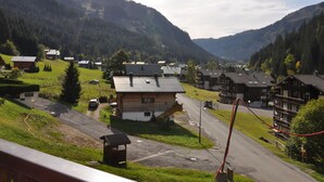 A mountain village with traditional wooden houses, a paved road, and a small parking area. - Cozy studio near center, balcony and parking (Châtel)