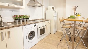 Cocina compacta con lavadora, microondas y zona de comedor con sillas.