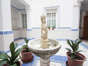 A courtyard with a stone fountain, potted plants, and a window with blinds. - Charming Studio in the Heart of Málaga, Ideal for Romantic Getaways (Málaga)