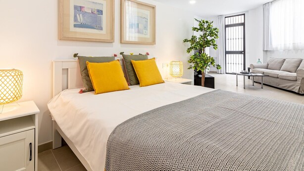 A modern hotel room with a large bed, two framed pictures on the wall, a potted plant, a sofa, and a coffee table. - Bright Loft in Málaga with A/C, Modern Kitchen, and High-Speed WiFi (Málaga)