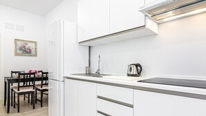 A modern kitchen with white cabinetry, a black countertop, and a kettle. There is a dining area with a table and chairs. - Bright Loft in Málaga with A/C, Modern Kitchen, and High-Speed WiFi (Málaga)