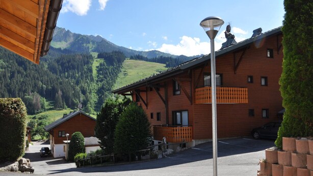 A rustic building with a wooden facade, a paved driveway, and a mountainous backdrop. - Apartment with Sunny Terrace in La Chapelle-d'Abondance (La Chapelle-d'Abondance)