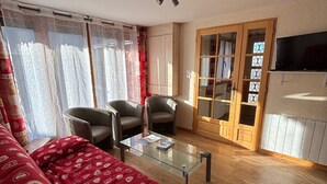 A living room with a glass coffee table, two armchairs, a red patterned sofa, and a wooden door with glass panels. - Apartment with Sunny Terrace in La Chapelle-d'Abondance (La Chapelle-d'Abondance)