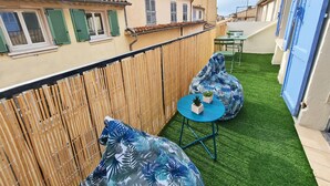 A balcony with a wooden fence, two blue chairs, a small table with a plant, and a green artificial lawn.