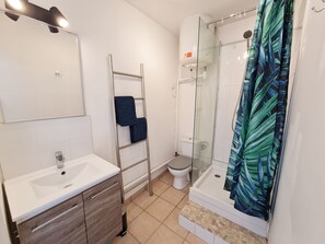 A bathroom with a white sink, a toilet, a glass shower enclosure, and a towel rack.