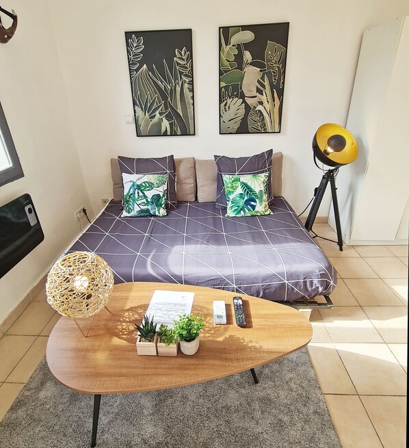 A modern bedroom with a bed, two wall-mounted artworks, a lamp, a coffee table with a plant, and a remote control.