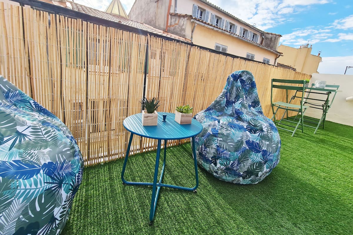 Kattohuoneistossa on terassi, jossa on keinonurmi, sininen pöytä, jossa on ruukkukasveja, vihreä tuoli ja bambuaita.