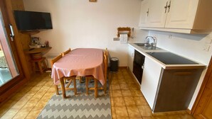 A compact kitchen with a dining table, a small sink, and a television mounted on the wall. - Charming apartment in Petit-Châtel, pets allowed (Châtel)