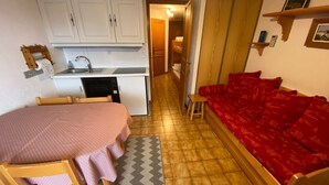 A compact room with a kitchenette, a dining area with a table and chairs, and a red sofa. - Charming apartment in Petit-Châtel, pets allowed (Châtel)