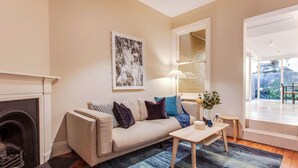 A living room with a beige sofa, a coffee table, and a fireplace. There is a large window with a view of the outdoors. - 2 mins walking to harbour bridge (Dawes Point)