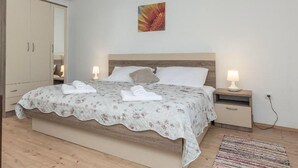 A bedroom with a bed, two bedside tables, a nightstand, a wooden floor, a wall-mounted painting, and a door. - Stunning home in Bila Vlaka (Bila Vlaka)