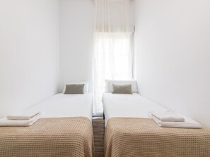 A hotel room with two single beds, white bedding, and a window with sheer curtains.