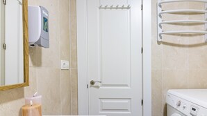 A bathroom with a white door, a hand dryer, a towel rack, a washing machine, and a candle on the sink. - Bright, Newly Renovated 2BR Apt in Historic Center Near Calle Larios (Málaga)