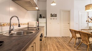 A modern kitchen with a stainless steel sink, a microwave, and a coffee maker. There is a wooden dining table with wicker chairs. - Bright, Newly Renovated 2BR Apt in Historic Center Near Calle Larios (Málaga)