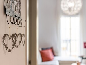 A room with a decorative wall hanging, a window with natural light, and a red pillow on a bed.