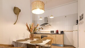 A modern kitchen with a dining area, featuring a central island, wicker furniture, and a hanging light fixture. - Bright, Newly Renovated 2BR Apt in Historic Center Near Calle Larios (Málaga)