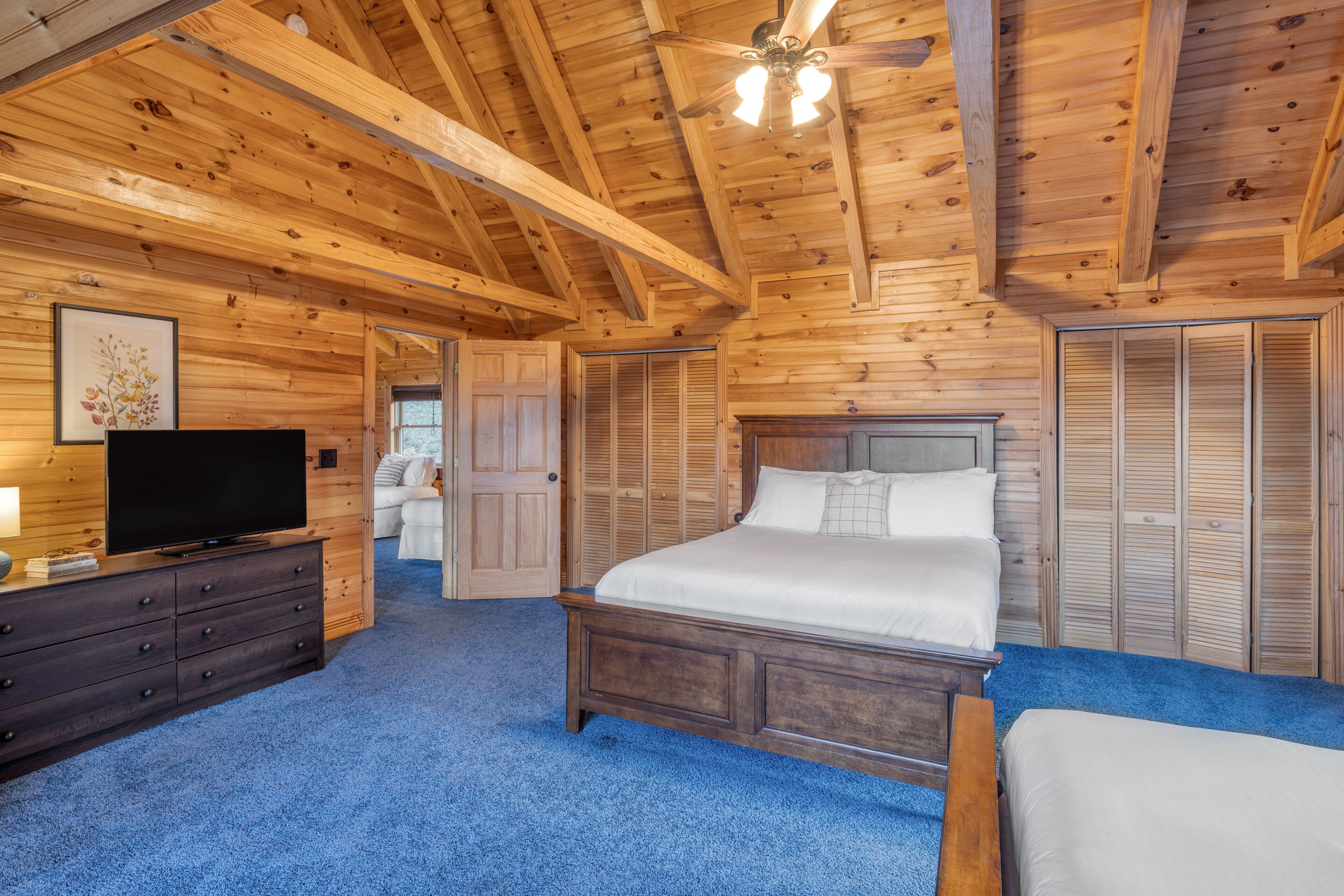Un dormitorio con paneles de madera, una cama, un aparador, un televisor y un ventilador de techo.