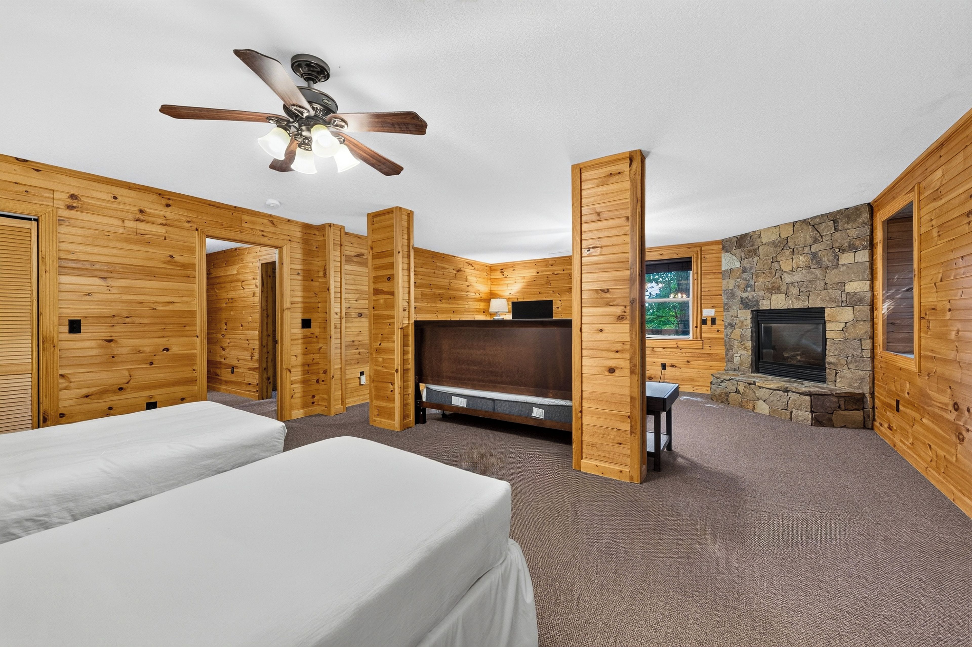 Une pièce aménagée dans le style d’un chalet en rondins, avec deux lits, une cheminée, un ventilateur de plafond et un mur en pierre.