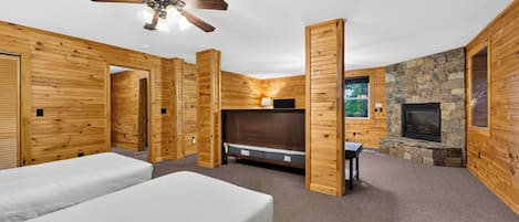 A log cabin-style room with two beds, a fireplace, a ceiling fan, and a stone wall.