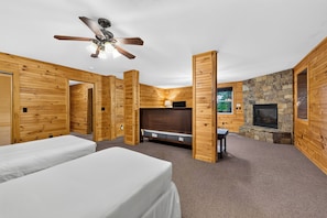 Une pièce aménagée dans le style d’un chalet en rondins, avec deux lits, une cheminée, un ventilateur de plafond et un mur en pierre.