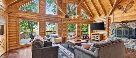 Gather beneath vaulted ceilings around the stone fireplace, with forest views beyond the windows.