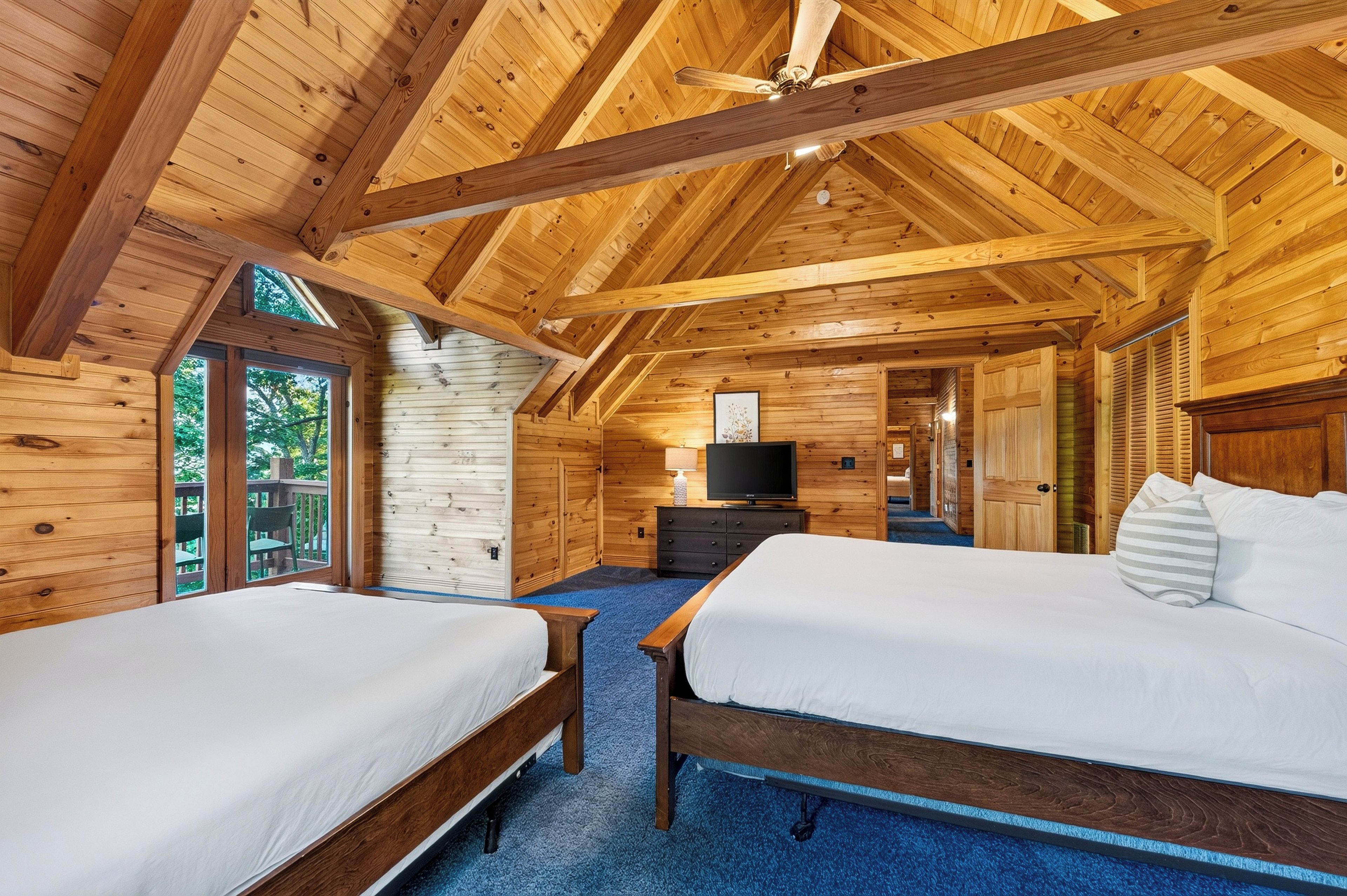 A wooden cabin room with two beds, a ceiling fan, and a TV.