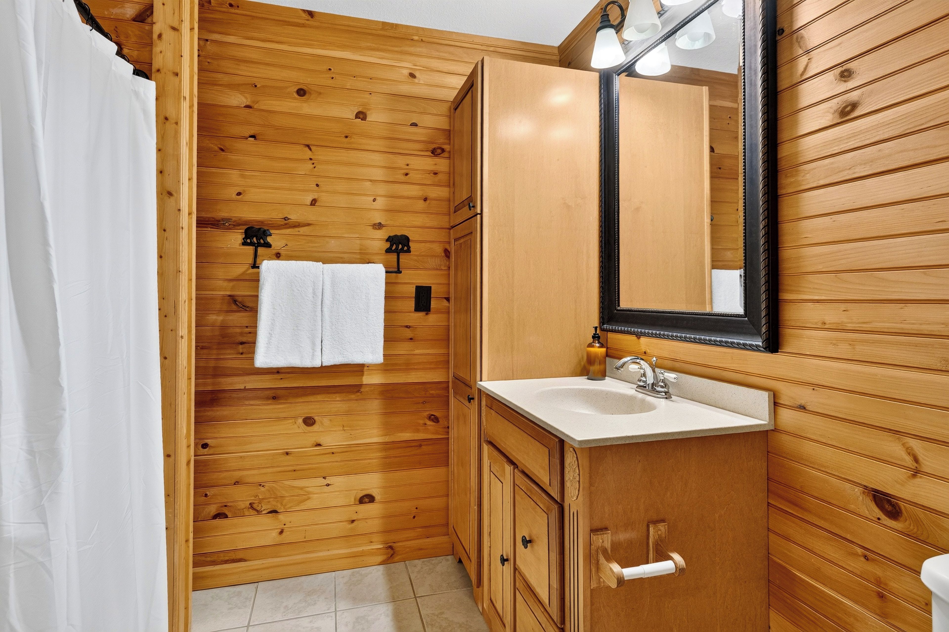 A wooden bathroom with a sink, mirror, towel rack, and toilet paper holder.