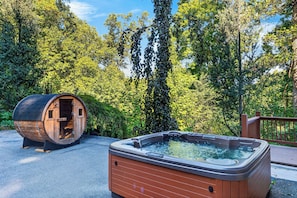 Un bain à remous et un tonneau en bois, le tout dans un cadre naturel agrémenté d’arbres.