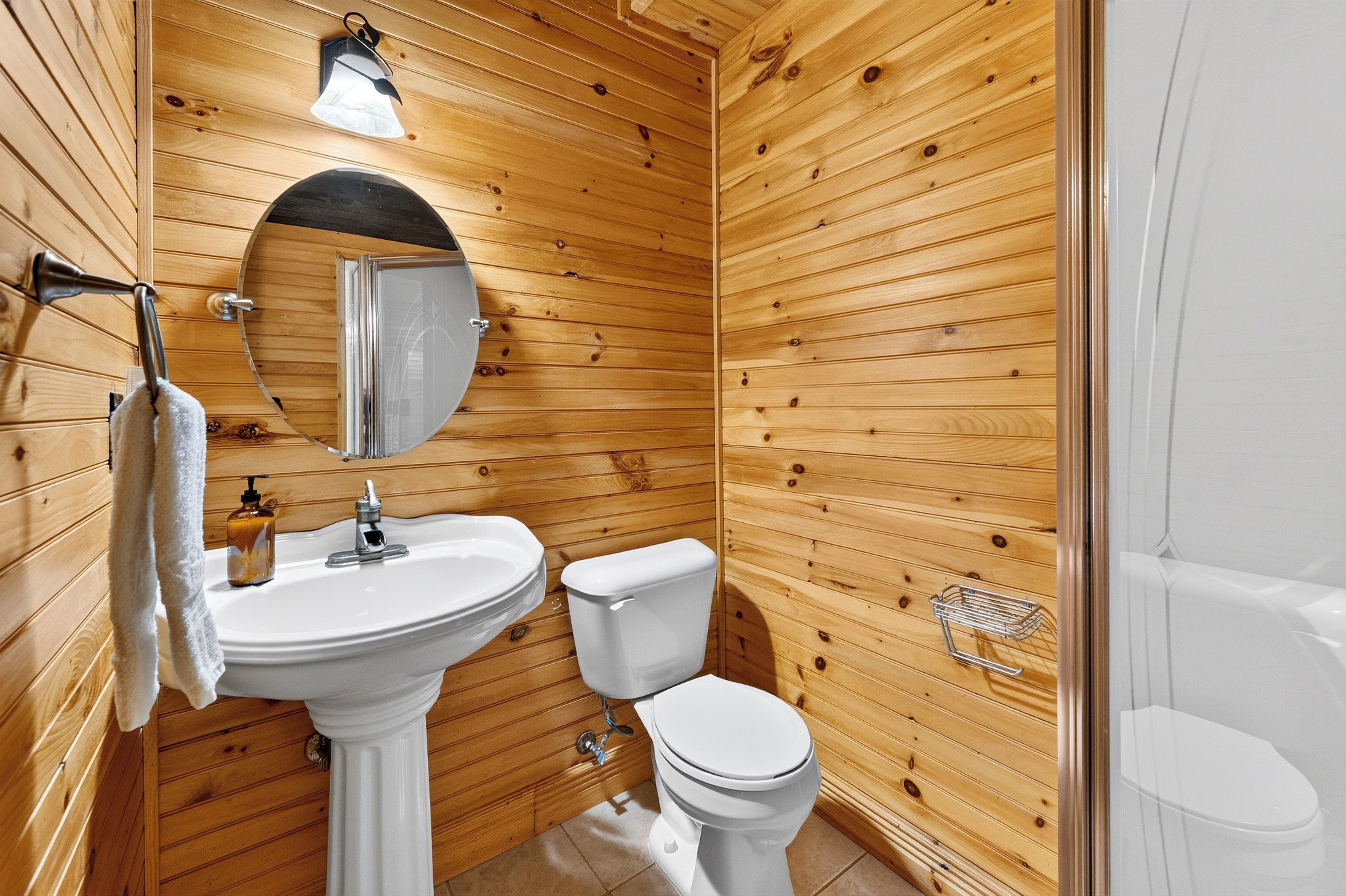 Un baño con paneles de madera, un lavabo pedestal, un inodoro y una zona de ducha.
