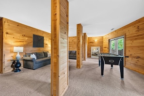 A cozy room with wooden walls, a sofa, a table, and a foosball table. - Sleeps 20 | Grand Mountain Lodge • Hot Tub + Sauna + Views | Mountain View Lodge (Asheville)