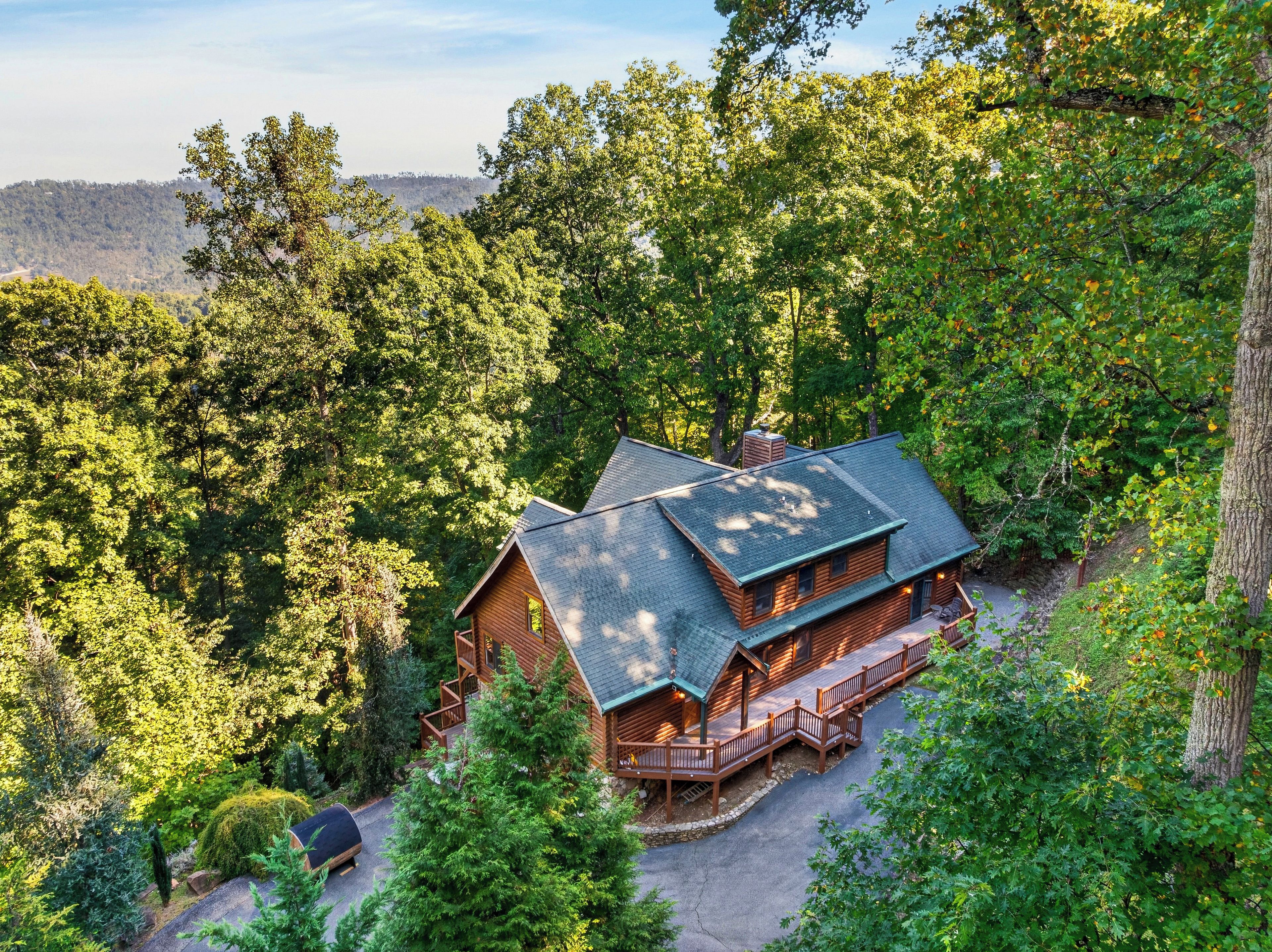 A cabin with a two-story structure, surrounded by dense forest, with a deck and a covered porch.