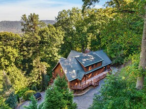 Une cabane à deux étages, entourée d’une forêt dense, dotée d’une terrasse et d’un porche couvert.