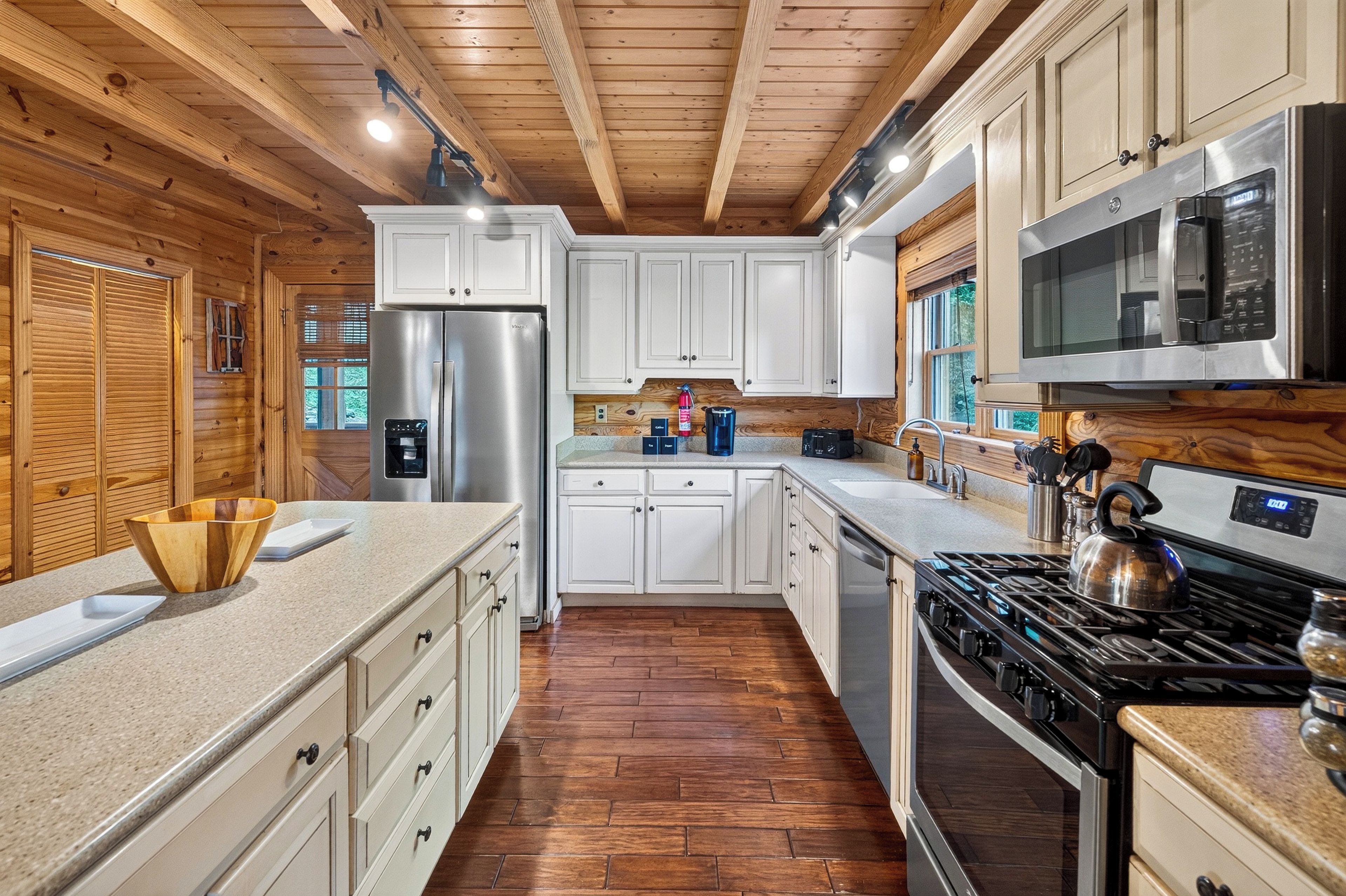 A kitchen with wooden ceiling beams, white cabinets, stainless steel appliances, and a herringbone-patterned floor.
