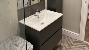 Ein modernes Badezimmer mit einem weißen Waschbecken, dunklen Schränken und einem Fischgrätenboden.