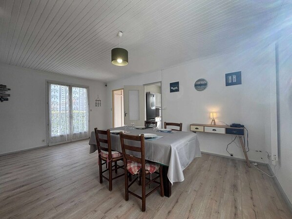 A dining area with a table set for four, wooden chairs, a hanging light fixture, and a view of the outdoors through a window.