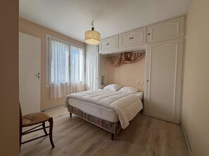 A bedroom with a bed, a chair, a wardrobe, and a window with curtains.